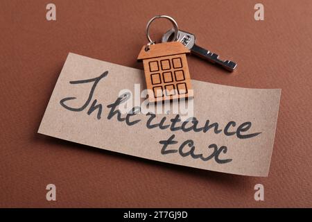 Scheda con frase Inheritance Tax e chiave con portachiavi a forma di casa su sfondo marrone, primo piano Foto Stock