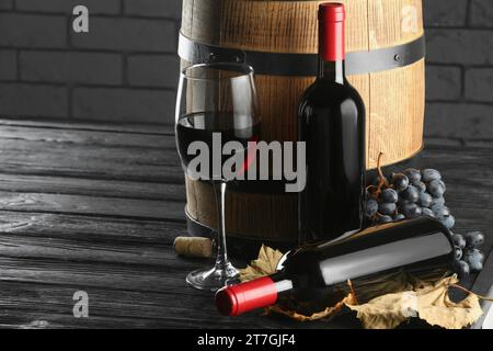 Vino delizioso, botte di legno, foglie secche e uva fresca su tavola nera, spazio per testo Foto Stock