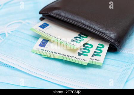 Nero uomo portafoglio con euro soldi dentro sul blu monouso maschere mediche viso. Permuta maschere mediche. Affari durante una pandemia o un'epidemia Foto Stock