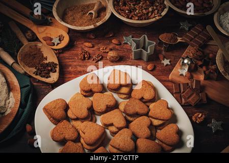 Biscotti a forma di cuore cotti su un piatto, ingredienti da forno, farina, zucchero, mandorle, noci, cioccolato, cannella, biscotti Foto Stock