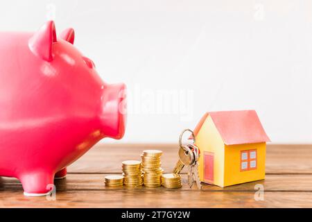 Casa con le monete chiave impilate oltre al piggybank Foto Stock