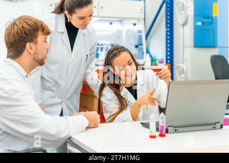 Una donna felice che utilizza un computer portatile mentre analizza i campioni in un laboratorio accanto ai colleghi Foto Stock