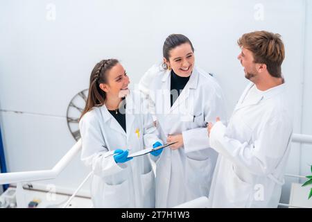 Vista laterale e vista elevata di tre giovani scienziati che ridono mentre lavorano in un laboratorio di ricerca sul cancro Foto Stock