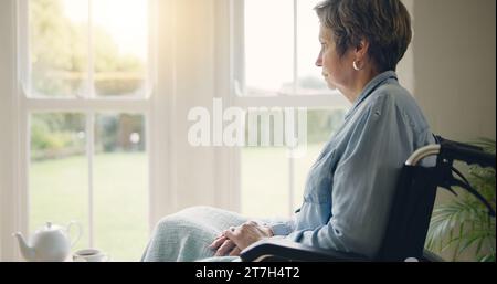 Sedia a rotelle, donna anziana o pensare alla memoria per finestra in casa di cura o pensione con depressione. Nostalgia del dolore, storia triste o maturità solitaria Foto Stock