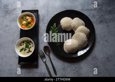 Spuntini dell'India meridionale idli sambar o idly sambhar preparati con riso fermentato al vapore e serviti con salsa di cocco e zuppa di verdure o sambar. Foto Stock