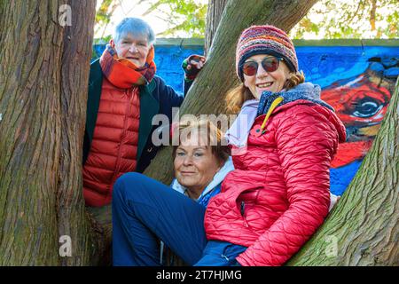 3 giocose donne anziane sopra i 60 alberi da arrampicata con graffiti sullo sfondo il giorno autunnale all'Hermitage Park, Helensburgh, Argyll e Bute, Scozia Foto Stock