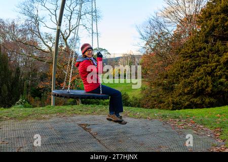 3 giocose donne anziane oltre i 60 anni si rilassano giocando a swing nel parco il giorno autunnale a Hermitage Park, Helensburgh, Argyll e Bute, Scozia Foto Stock