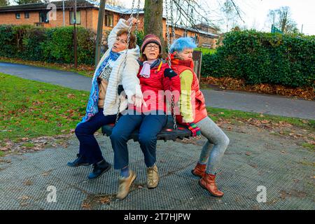 3 giocose donne anziane oltre i 60 anni si rilassano giocando a swing nel parco il giorno autunnale a Hermitage Park, Helensburgh, Argyll e Bute, Scozia Foto Stock