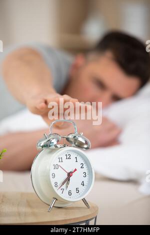 un uomo sdraiato sul letto e che ferma la sveglia Foto Stock