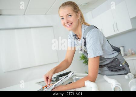 l'idraulico donna felice sta riparando il lavandino della cucina Foto Stock