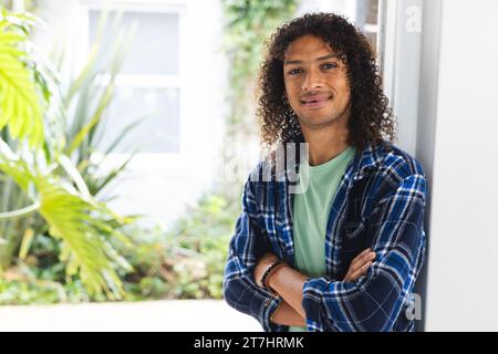 Felice uomo birazziale con lunghi capelli ricci scuri che sorridono nel soleggiato salotto di casa Foto Stock