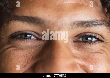 Occhi di felice uomo birazziale con lunghi capelli ricci scuri che ridono nel soleggiato salotto di casa Foto Stock