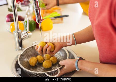 Mani di felice bionda donna caucasica lavando le patate in una cucina soleggiata a casa Foto Stock