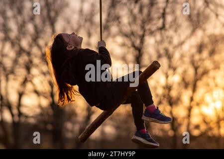 Ritratto di una bambina felice che altalena sulla natura, nel parco, nel villaggio, nel campo per bambini sullo sfondo di alberi. gam all'aperto Foto Stock