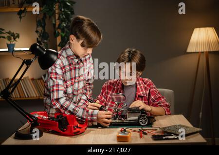 Ragazzi adolescenti intelligenti che studiano elettronica e fili per saldatura nel loro progetto di robotica scientifica. Istruzione a casa Foto Stock