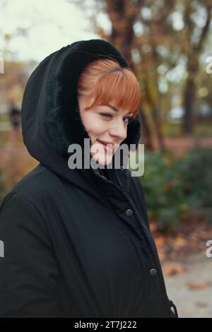 Donna rossa che fa l'occhiolino in cappotto con cappuccio in autunno durante la passeggiata nella foresta Foto Stock