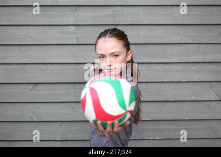 La ragazza adolescente tiene la pallavolo con la mano pronta a servire, fissando il copyspace della telecamera Foto Stock