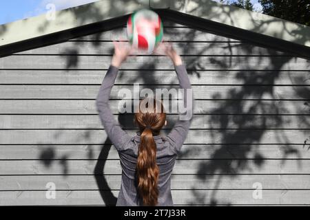 La ragazza adolescente pratica i tiri di pallavolo: Prepara la palla con entrambe le mani sopra la testa, la palla si sfoca Foto Stock