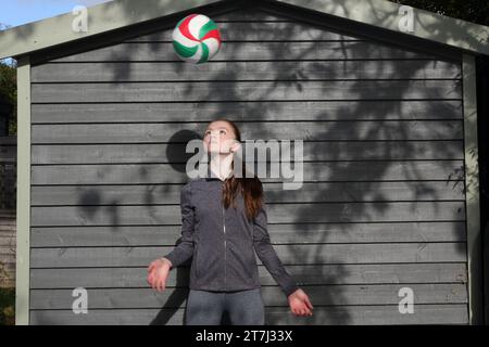 La ragazza adolescente pratica i tiri di pallavolo e tiene gli occhi sulla palla mentre galleggia più in alto Foto Stock