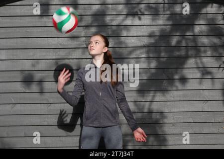 La ragazza adolescente pratica i tiri di pallavolo lanciando la palla nella mano destra e tenendo gli occhi sulla palla Foto Stock