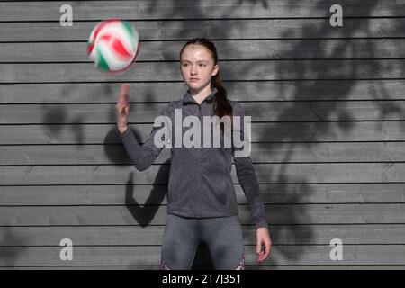 La ragazza adolescente pratica i tiri di pallavolo e lancia la palla in aria con palline sfocate e sfocate a mano Foto Stock
