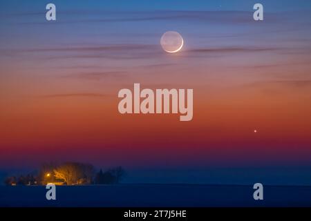 La sottile luna a mezzaluna di un giorno, appena sopra Giove, ambientata la sera del 22 marzo 2023. Il bagliore Earthshine è evidente sul lato oscuro di Foto Stock