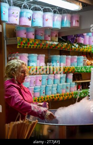 Trasformare i sogni di zucchero in realtà: Una donna abile fa girare la magia in una bancarella di strada, creando il dolce fascino delle caramelle di cotone sotto il bagliore urbano. Foto Stock