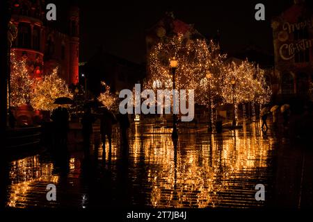 La magia delle feste si svolge mentre le luci natalizie baciate dalla pioggia adornano gli alberi, proiettando riflessi scintillanti sul terreno bagnato sotto l'incantevole velo di una vittoria Foto Stock