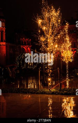 Natale baciato dalla pioggia: La magia notturna si svolge mentre le luci festive ballano sugli alberi bagnati, gettando incantevoli riflessi sul terreno scintillante. Foto Stock