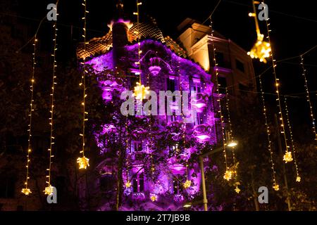Casa Batlló, immersa in tonalità viola, si erge adornata da incantevoli luci natalizie, che creano una magia nella vivace strada sottostante Foto Stock