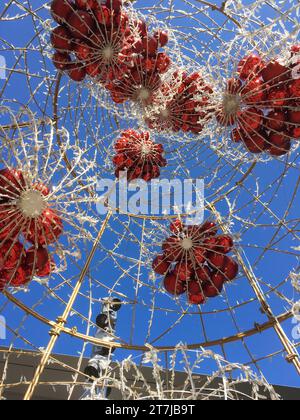 Baldacchino di Natale: All'interno di un maestoso albero adornato di bauble rossi e luci, l'atmosfera festosa incontra il tranquillo cielo blu in un giorno accattivante Foto Stock