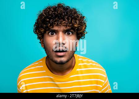Ritratto fotografico di un giovane attraente che si prende gioco del viso confuso indossa abiti gialli a righe alla moda isolati su sfondo color acquamarina Foto Stock