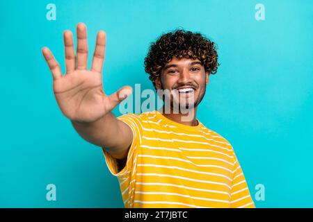 Ritratto fotografico di un bel giovane ragazzo che si allunga la mano, vestito elegante vestito giallo a righe isolato su sfondo di colore ciano Foto Stock