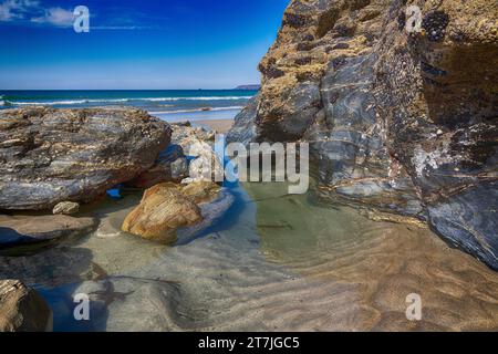 Vista bassa marea - Rocks a vista, piscina rocciosa, spiaggia sabbiosa e vista sul mare a Portreath Beach, Cornovaglia, con cielo blu all'inizio dell'estate. Foto Stock