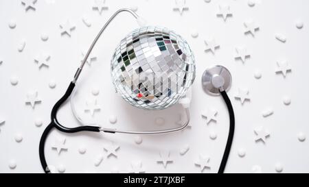 Banner medico natalizio.primo piano di stetoscopio, disco ball, stelle e pillole su sfondo bianco, vista dall'alto, piatto, copia spazio.anno nuovo o Natale par Foto Stock