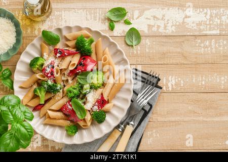 Penne per pasta integrale con broccoli e peperoni rossi grigliati e su un tavolo rustico in legno chiaro. Pasta vegana. Cucina tradizionale italiana Foto Stock