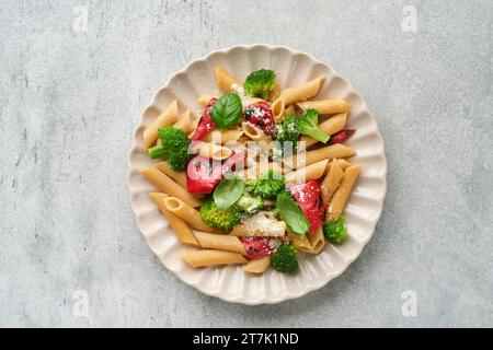 Penne per pasta integrale con broccoli e peperone rosso grigliato e su sfondo grigio chiaro ardesia, pietra o cemento. Pasta vegana. Tradizionale Itali Foto Stock