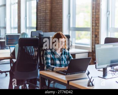 Una donna d'affari giovane e di successo dai capelli arancioni si impegna in un ufficio moderno, dimostrando la sua sicurezza e dinamicità Foto Stock