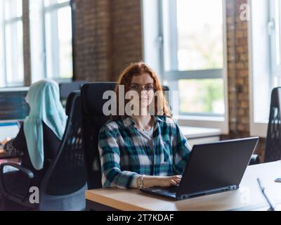 Una donna d'affari giovane e di successo dai capelli arancioni si impegna in un ufficio moderno, dimostrando la sua sicurezza e dinamicità Foto Stock