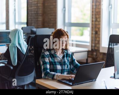 Una donna d'affari giovane e di successo dai capelli arancioni si impegna in un ufficio moderno, dimostrando la sua sicurezza e dinamicità Foto Stock