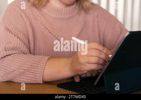 Mano di una donna irriconoscibile che usa un tablet grafico con penna stilo in un bar. Foto ritagliata di una donna che lavora su un display digitale touchscreen de Foto Stock