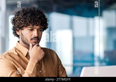 Uomo d'affari serio all'interno dell'ufficio sul posto di lavoro, si concentra e si concentra sulla risoluzione dell'attività corrente, il dipendente utilizza un notebook al lavoro, legge la documentazione online. Foto Stock