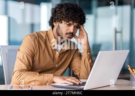 Uomo d'affari serio all'interno dell'ufficio sul posto di lavoro, si concentra e si concentra sulla risoluzione dell'attività corrente, il dipendente utilizza un notebook al lavoro, legge la documentazione online. Foto Stock