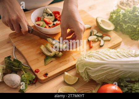 Signora che affetta un avocado su un tavolo di legno con verdure fresche Foto Stock