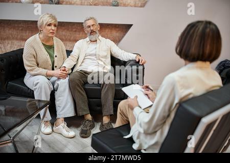 coppia sposata di mezza età che discute di problemi coniugali seduto sul divano di pelle vicino al terapeuta Foto Stock