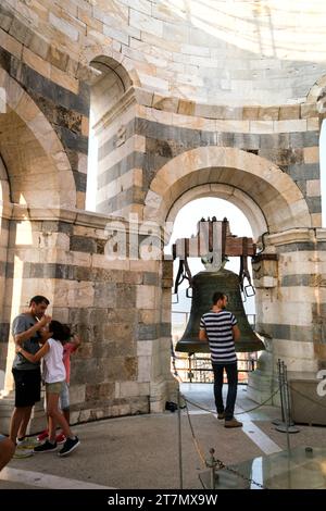 I turisti che visitano il campanile in cima alla Torre Pendente di Pisa proteggono le loro orecchie mentre un uomo suona la gigantesca campana di metallo, Pisa, Italia, Europa Foto Stock