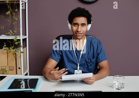 Ritratto frontale di un giovane arabo come medico che indossa cuffie a cancellazione di rumore sul posto di lavoro e parla con il paziente, spazio per le copie Foto Stock