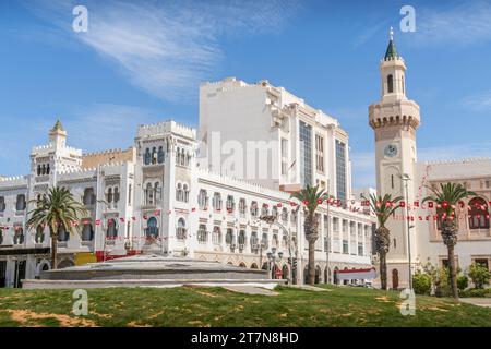Gli edifici di architettura coloniale dipinti di bianco nel centro di Sfax, in Tunisia, con le bandiere tunisine, gli splendidi balconi e il piccolo parco. Foto Stock