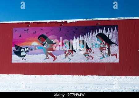 Murale su palo rosso edificio di donne native con disegni geometrici tribali che si avvicinano a un corvo nero in un giorno d'inverno, Yellowknife, Northwest Territor Foto Stock