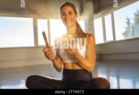Donna che tiene la ciotola e il mazzuolo in palestra, soleggiata, meditazione pacifica Foto Stock